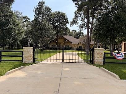 Black iron estate gate with stone pillars and fence on rural property in Montgomery County TX